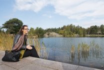 Mulher adulta média sentada junto ao lago, foco seletivo — Fotografia de Stock