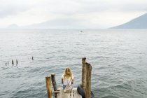 Вид ззаду жінки, що сидить на пірсі, вибірковий фокус — стокове фото