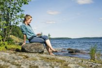 Donna adulta con tablet digitale di fronte al lago in Finlandia — Foto stock