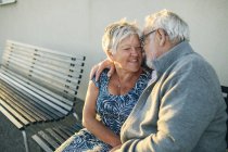 Старшая пара обнимается на скамейке, фокусируется на переднем плане — стоковое фото