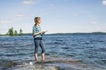 Mitte erwachsene Frau benutzt digitales Tablet in der Nähe eines Sees in Finnland — Stockfoto