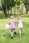 Вид сзади на детей, бегающих с воздушными шарами в парке — стоковое фото