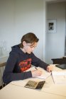 Хлопчик-підліток робить домашнє завдання вдома, зосередитися на передньому плані — стокове фото