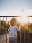 Девушка стоит на балконе на закате, фокусируется на переднем плане — стоковое фото