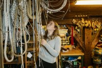 Teenage girl reaching up to touch ropes in rope maker store — Stock Photo