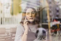 Woman using smart phone behind cafe window, selective focus — Stock Photo