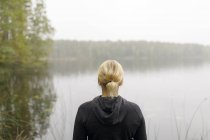 Vista trasera de la mujer rubia de pie junto al lago, se centran en primer plano - foto de stock