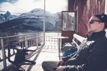Homem sentado na varanda com montanhas cobertas de neve no fundo em Troms Fylke, Noruega — Fotografia de Stock