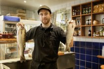 Portrait of fishmonger holding fish in store, selective focus — Stock Photo