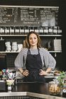 Portrait of barista with hands on hips behind counter in cafe — Stock Photo