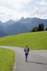 Vue arrière de la jeune fille marchant le long de la route rurale à Vorarlberg, Autriche — Photo de stock