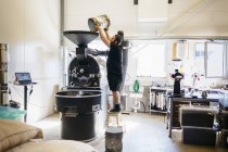 Homem derramando grãos de café na máquina de torrefação — Fotografia de Stock