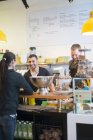 Woman buying coffee in cafe from two bartenders — Stock Photo