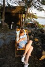 Junge Frau sitzt auf Liegestuhl und benutzt Smartphone — Stockfoto