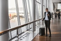 Mulher com mala e telefone inteligente no aeroporto — Fotografia de Stock