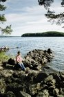 Mulher sentada na rocha por lago — Fotografia de Stock