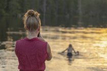 Mujer fotografiando chica en el lago al atardecer, enfoque selectivo - foto de stock