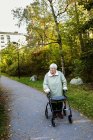 Пожилая женщина с помощью шагающей рамы и прогулки в парке — стоковое фото