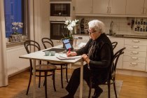 Пожилая женщина с ноутбуком на кухне — стоковое фото