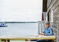 Mujer madura sentada en la mesa de picnic junto a la cabaña de madera - foto de stock