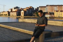 Man sitting on boardwalk using smartphone and smiling at sunny day — Stock Photo