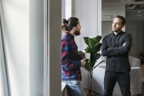 Молоді співробітники чоловічої статі стоять разом і розмовляють вікном — стокове фото