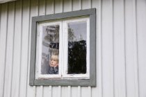 Petit garçon mignon dans la fenêtre de la maison — Photo de stock