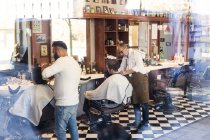 Veja através da janela de barbeiros cortando os cabelos dos clientes — Fotografia de Stock