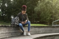 Дівчина-підліток сидить і використовує смартфон у парку — стокове фото