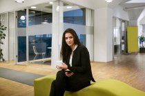 Junge Frau hält Smartphone und sitzt auf Bürosofa — Stockfoto