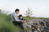 Padre e figlio utilizzando uno smartphone sull'erba — Foto stock
