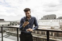Молодой человек смотрит на сотовый телефон на балконе — стоковое фото
