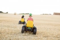 Дети катаются на игрушечных тракторах в поле, избирательный фокус — стоковое фото