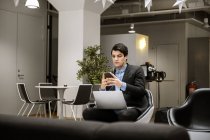 Young man in earphones using smartphone and laptop in office — Stock Photo