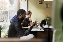 Visão lateral de homens jovens sentados e usando dispositivos digitais no café — Fotografia de Stock