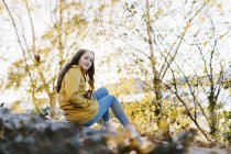 Girl wearing yellow raincoat sitting by trees — Stock Photo