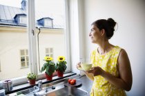 Woman drinking coffee and looking through window — Stock Photo