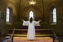 Священик у білому одязі, що стоїть біля церкви, вид ззаду — стокове фото