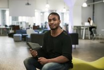 Mitte erwachsener Mann hält Laptop in der Hand und schaut in die Kamera, während er im Büro auf dem Sofa sitzt — Stockfoto