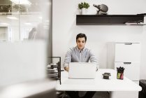 Young man using laptop at desk in office — Stock Photo