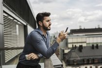 Giovane uomo guardando il telefono cellulare sul balcone — Foto stock