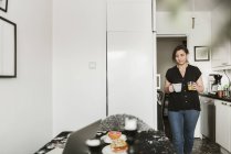 Mujer joven llevando tazas en la cocina - foto de stock