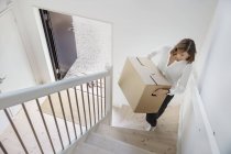 Woman carrying cardboard box up staircase — Stock Photo