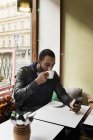 Jovem com telefone inteligente bebendo café no café — Fotografia de Stock