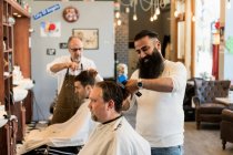 Barbers cutting customers hair in barbershop — Stock Photo