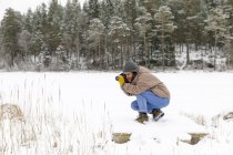 Mujer agachada tomando fotos en la nieve - foto de stock