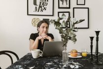 Junge Frau benutzt Laptop beim Frühstück — Stockfoto