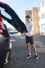 Full length view of preteen boy closing car boot — Stock Photo