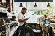 Homme d'âge moyen travaillant dans un café, utilisant un téléphone intelligent — Photo de stock