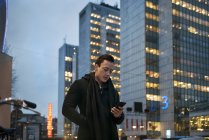 Молодой человек использует мобильный телефон во время прогулки по городской улице — стоковое фото